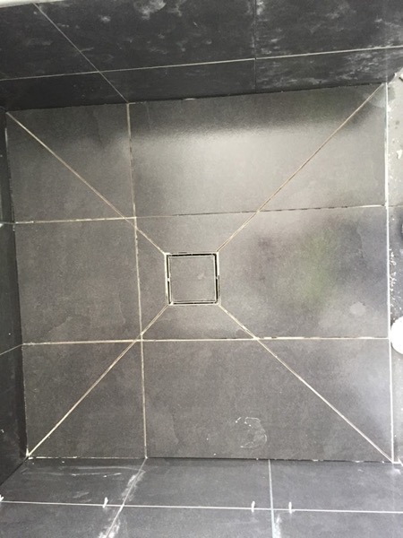A dark tiled floor with a square stainless floor waste set into the centre