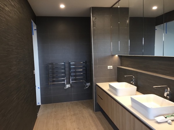 A bathroom with charcoal tiled walls, a timber vanity and two basins