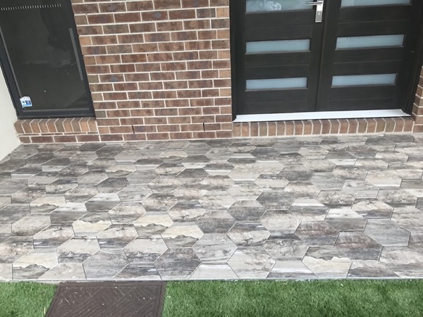 A hexagon stone-look tiled porch running up to a brick house and dark front doors