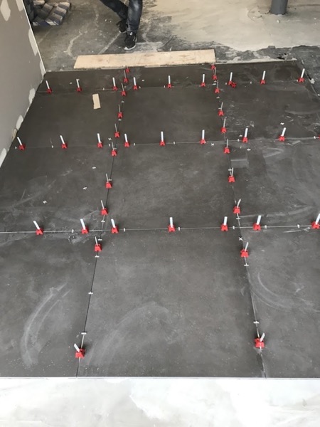 A floor part-tiled with red levelling clips holding the tiles flush at every joint