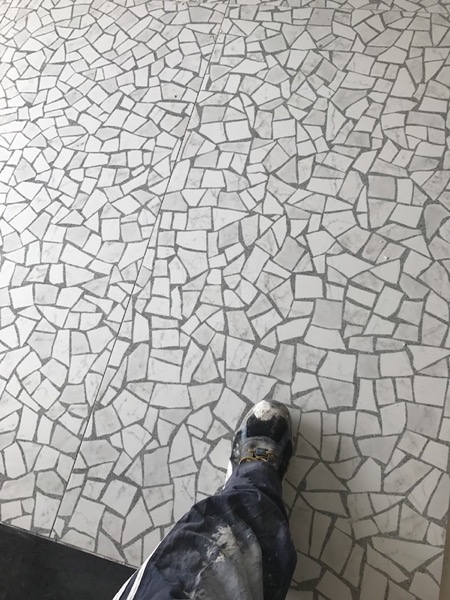 A floor of hand-cut white marble crazy paving with a work boot at the edge