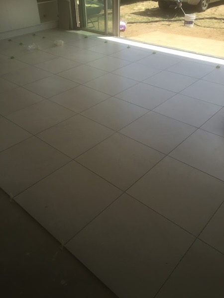 Beige floor tiles laid across a room in a straight stack bond