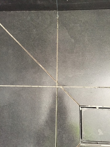 A dark tiled shower floor falling to a square floor waste