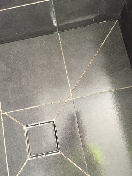 Dark textured tiles meeting on a diagonal joint at a stainless floor waste