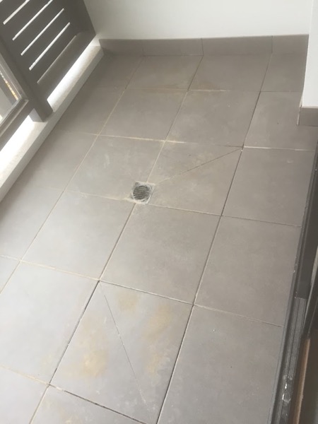 A pale tiled floor with a round floor waste beside a full-height window
