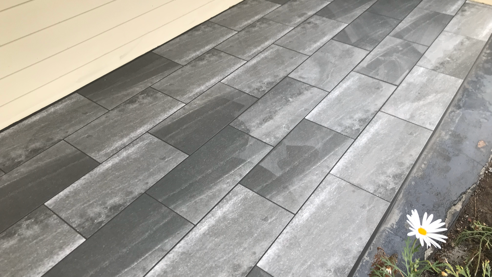 Grey plank-format outdoor tiles laid in a staggered pattern beside a garden edge