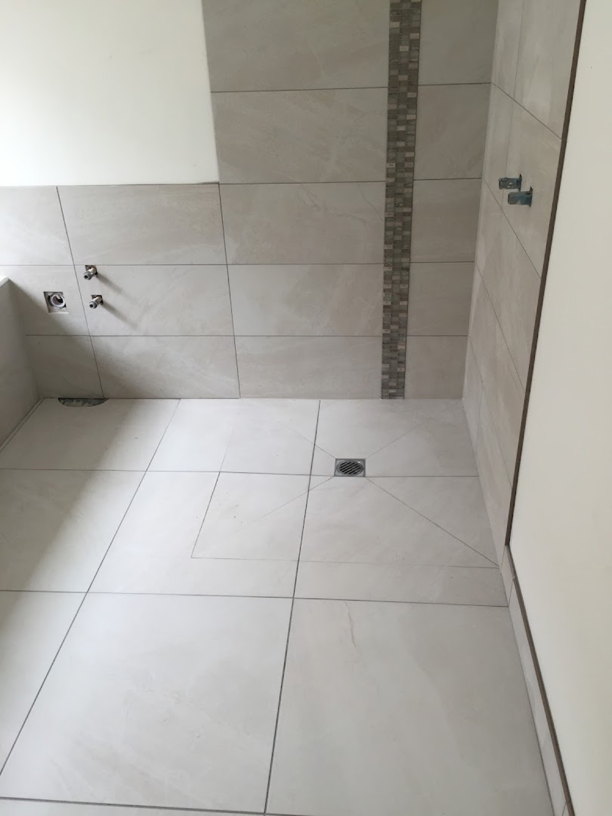 A tiled shower base with a square floor waste and a mosaic feature strip