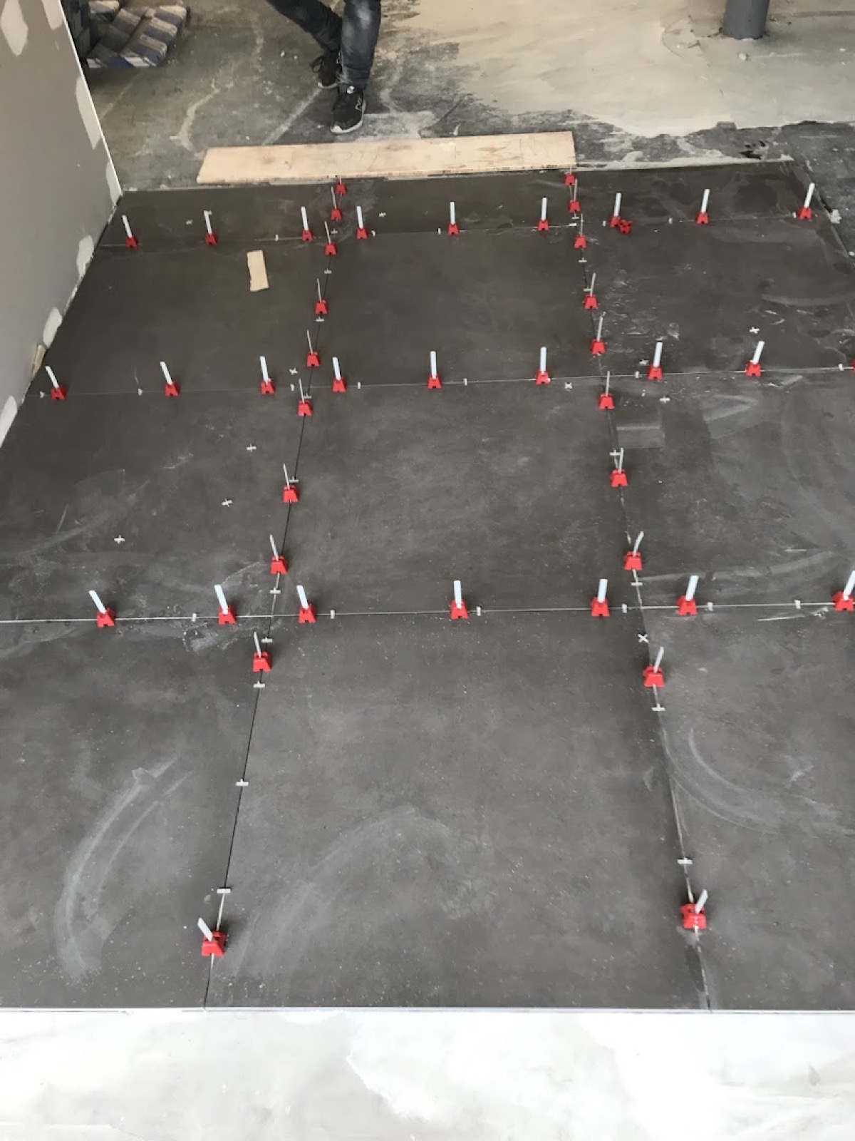 A floor part-tiled with levelling clips holding the tiles flush at every joint