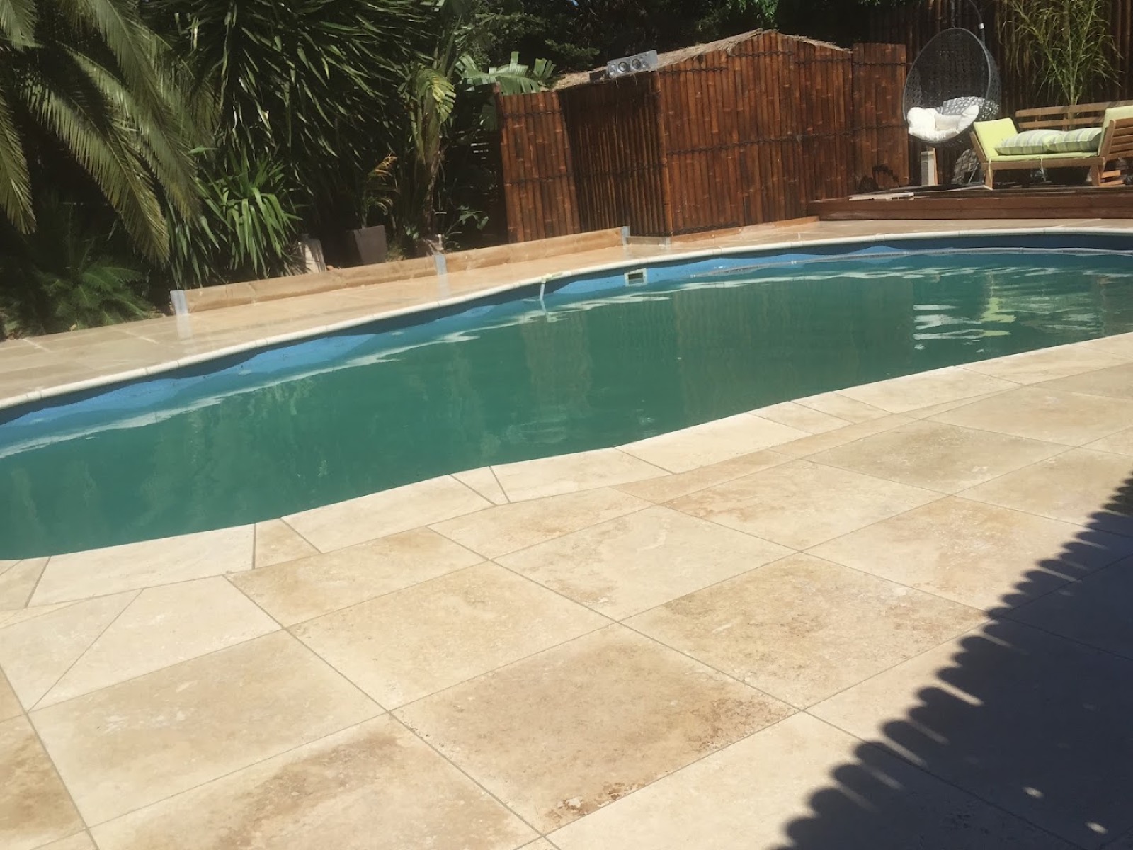 Travertine paving laid around the curved edge of a backyard pool