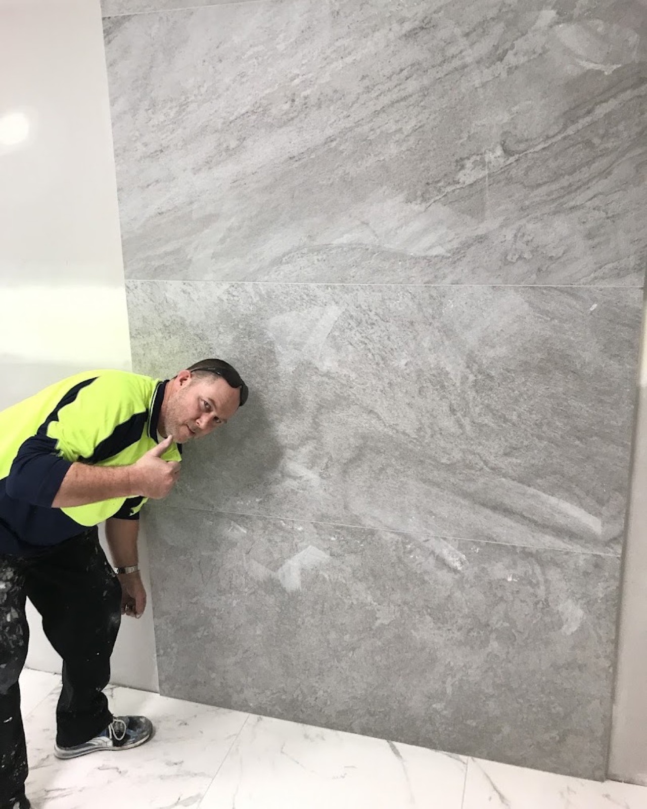 A tiler in a hi-vis shirt standing beside a wall of large-format stone-look tiles