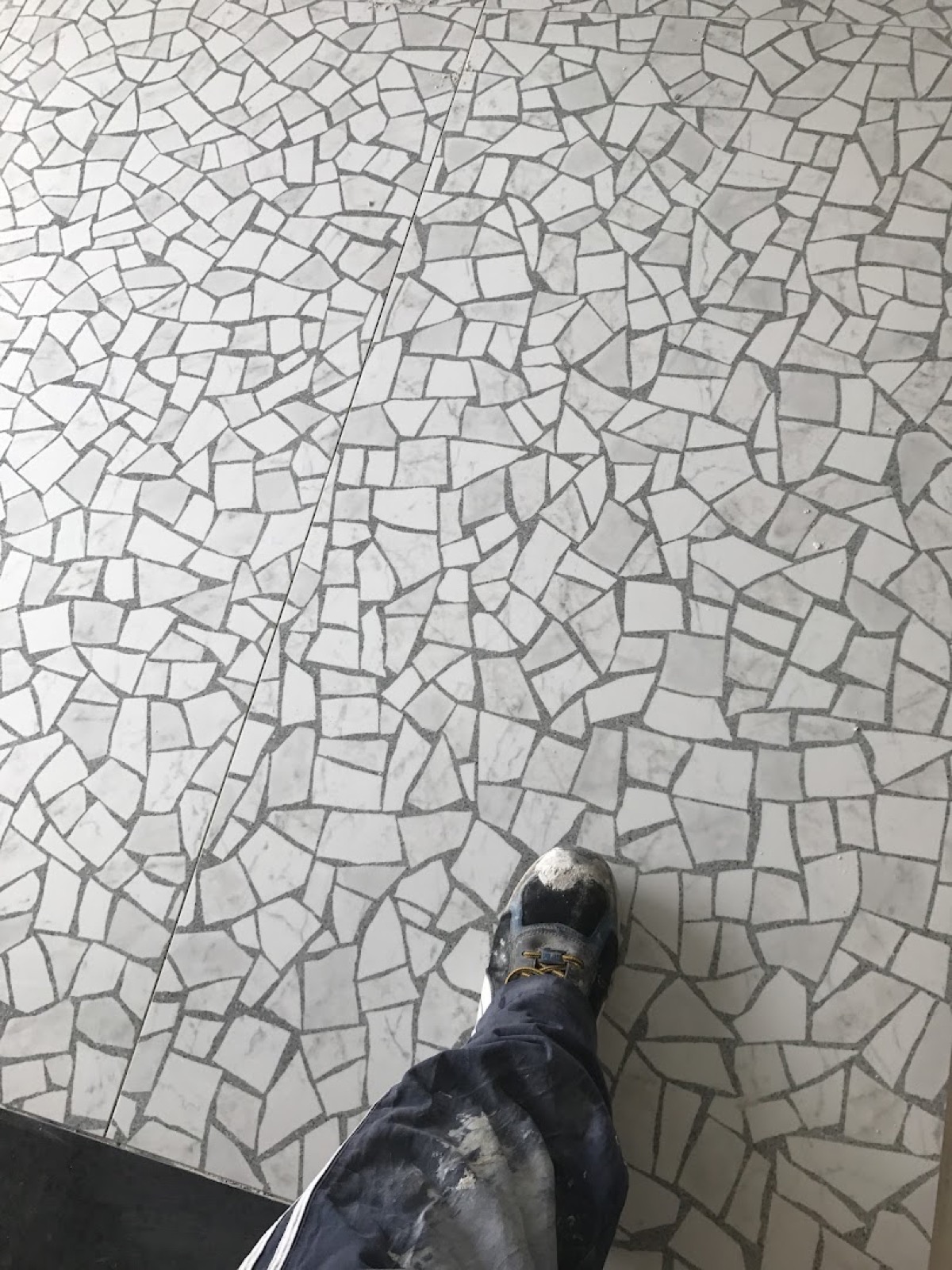 A floor of hand-cut white marble crazy paving with a work boot at the edge