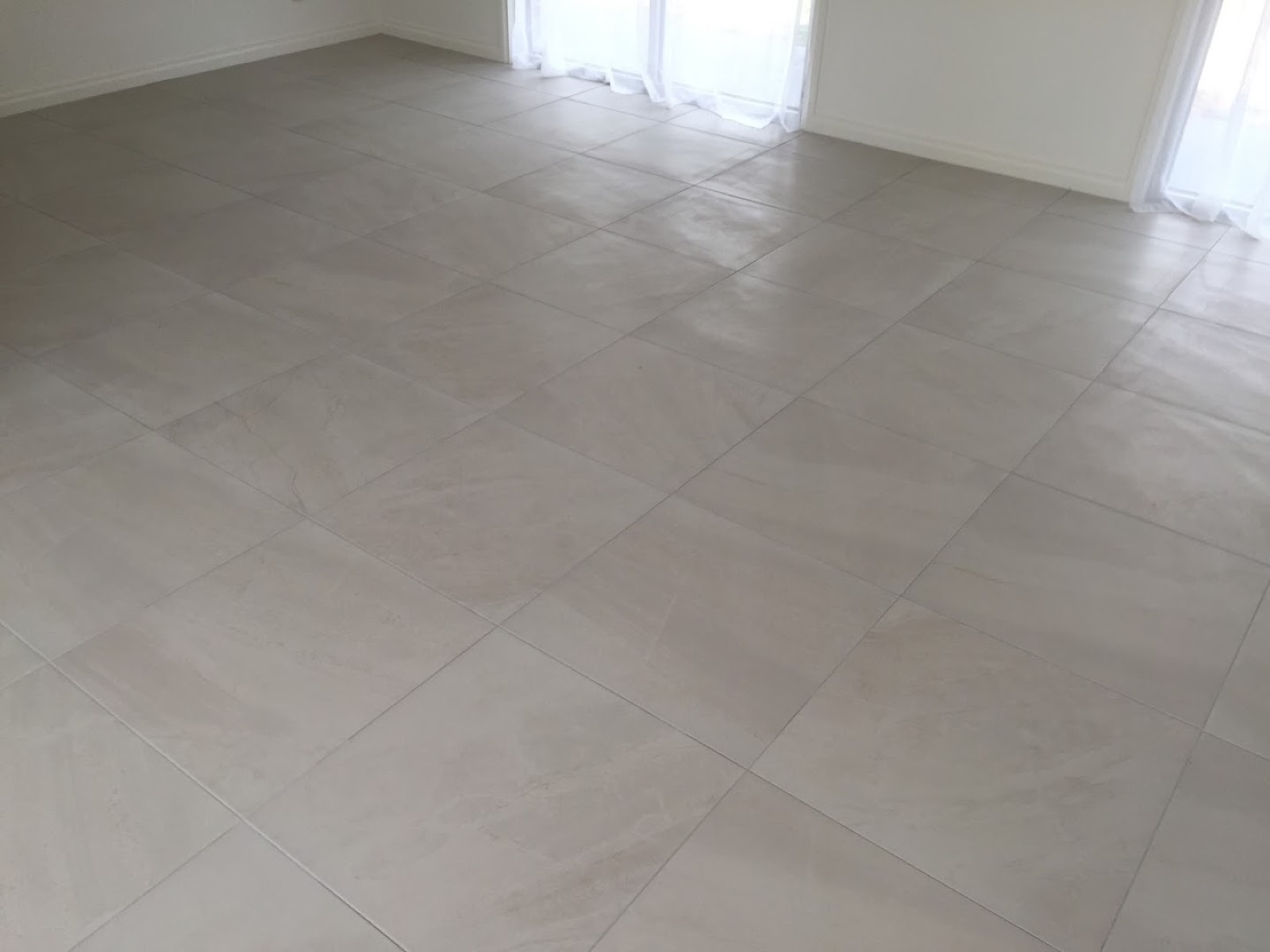 A living area floor freshly tiled in pale square tiles up to the skirting