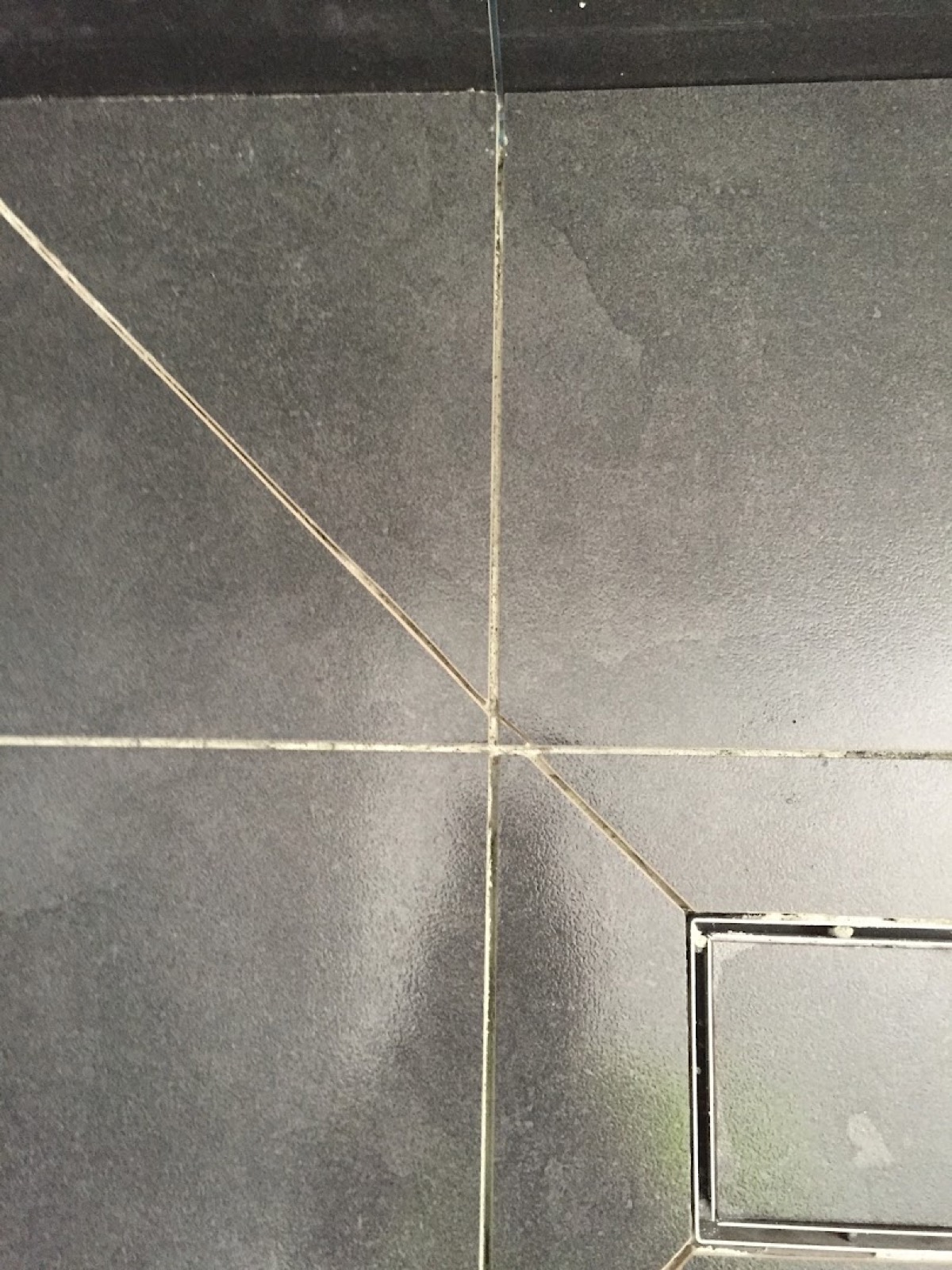 A dark tiled shower floor falling to a square floor waste