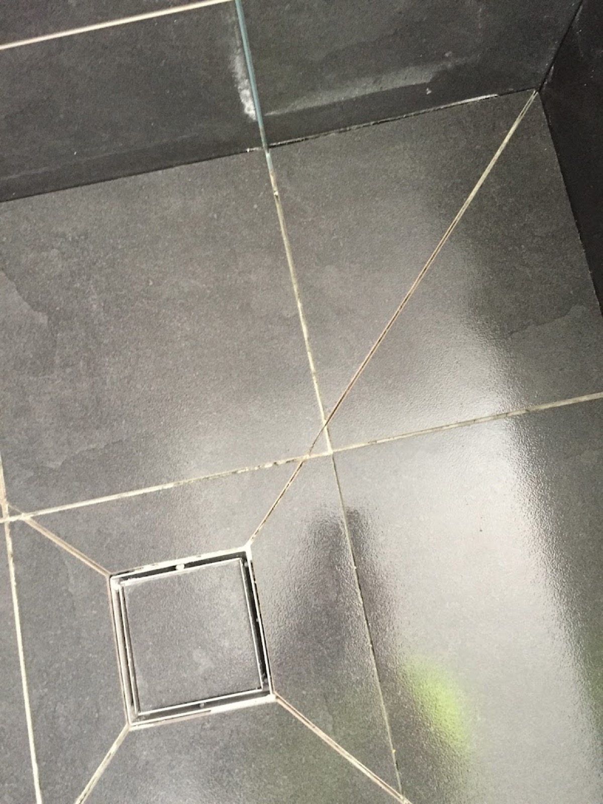 Pale grout lines running between dark floor tiles around a square floor waste